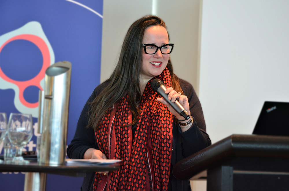 A woman holds a microphone and speaks at a lectern.