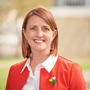 Louise smiling at the camera. She is wearing a red blazer.