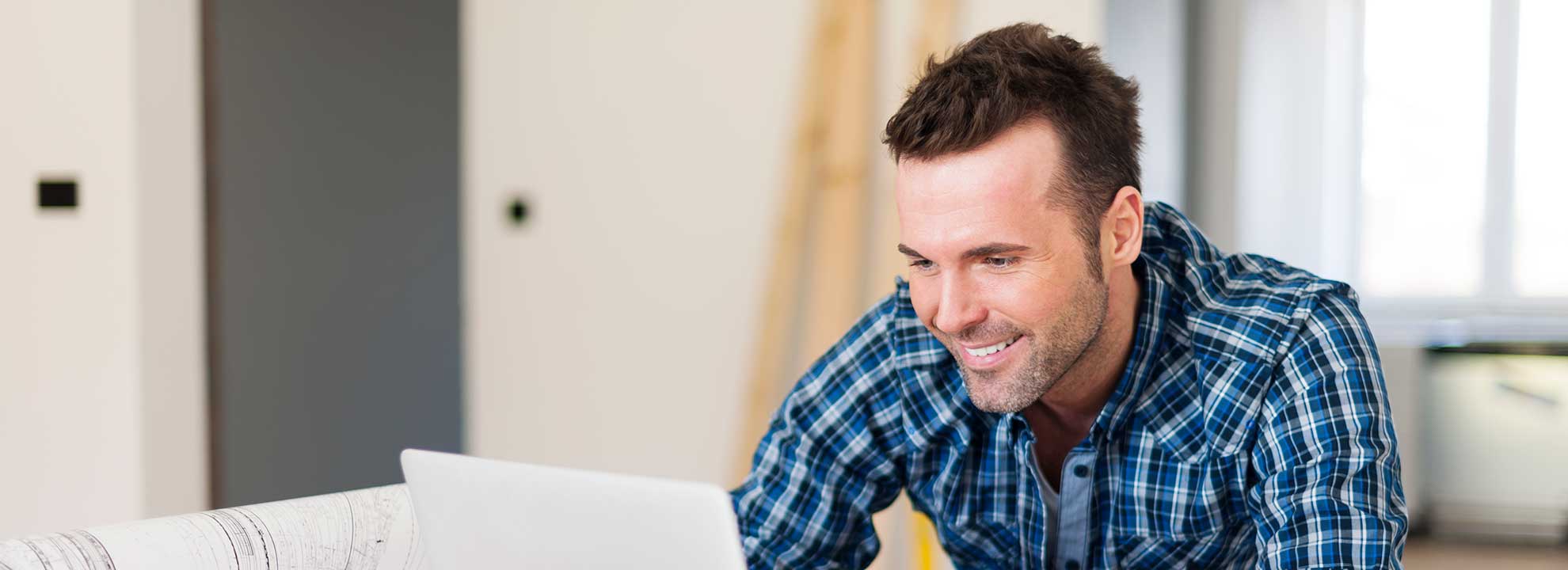 A tradesman sitting at a desk looking at a laptop computer.