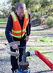 A GWW worker connecting to a water hydrant. An arrow is superimposed over him indicating to turn anti-clockwise.