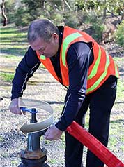 A GWW worker connecting to a water hydrant. An arrow is superimposed over him indicating to turn clockwise when disconnecting.