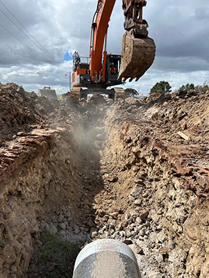 A ground view with the new water main in the foreground and a excavator in the background.