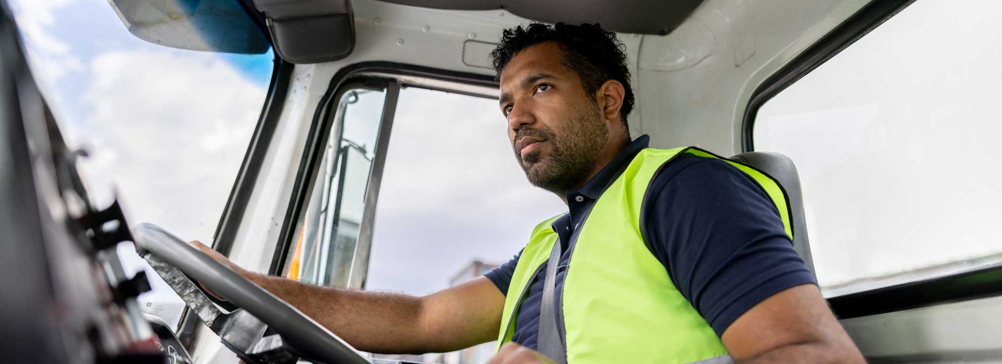 A cabin view of a person wearing a hi-vis vest driving a water carting truck.