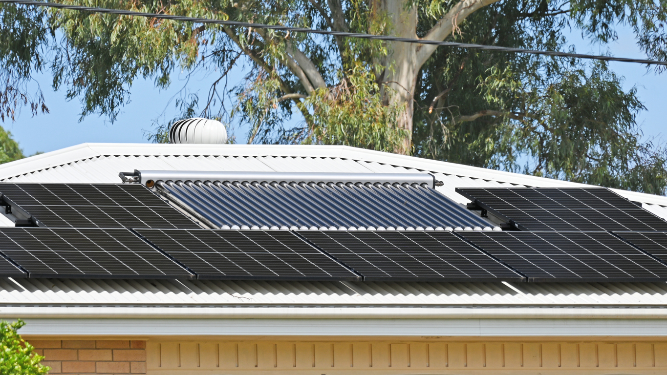 Solar hot water panels installed on a residential house roof against a clear sky.