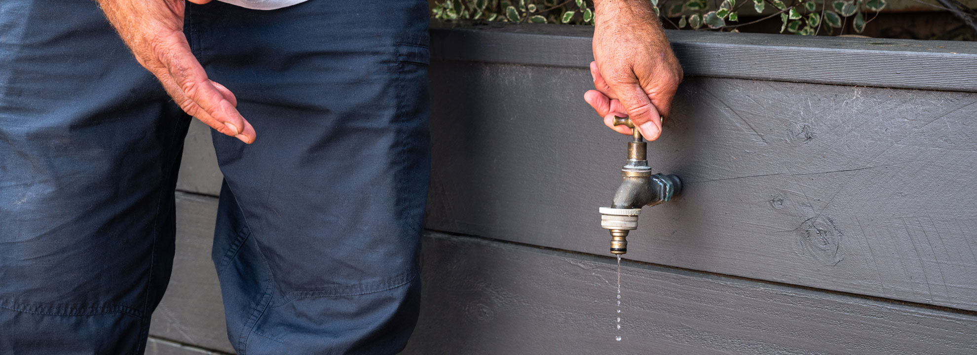 A hand turning a water tap on, the tap has a small stream of water coming out of it. 