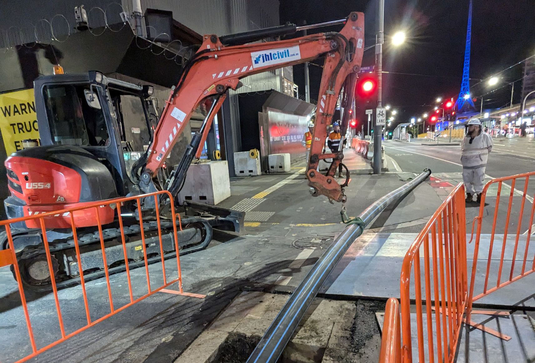 Construction works taking place at night time, including a digger and the Melbourne Arts Centre in the background