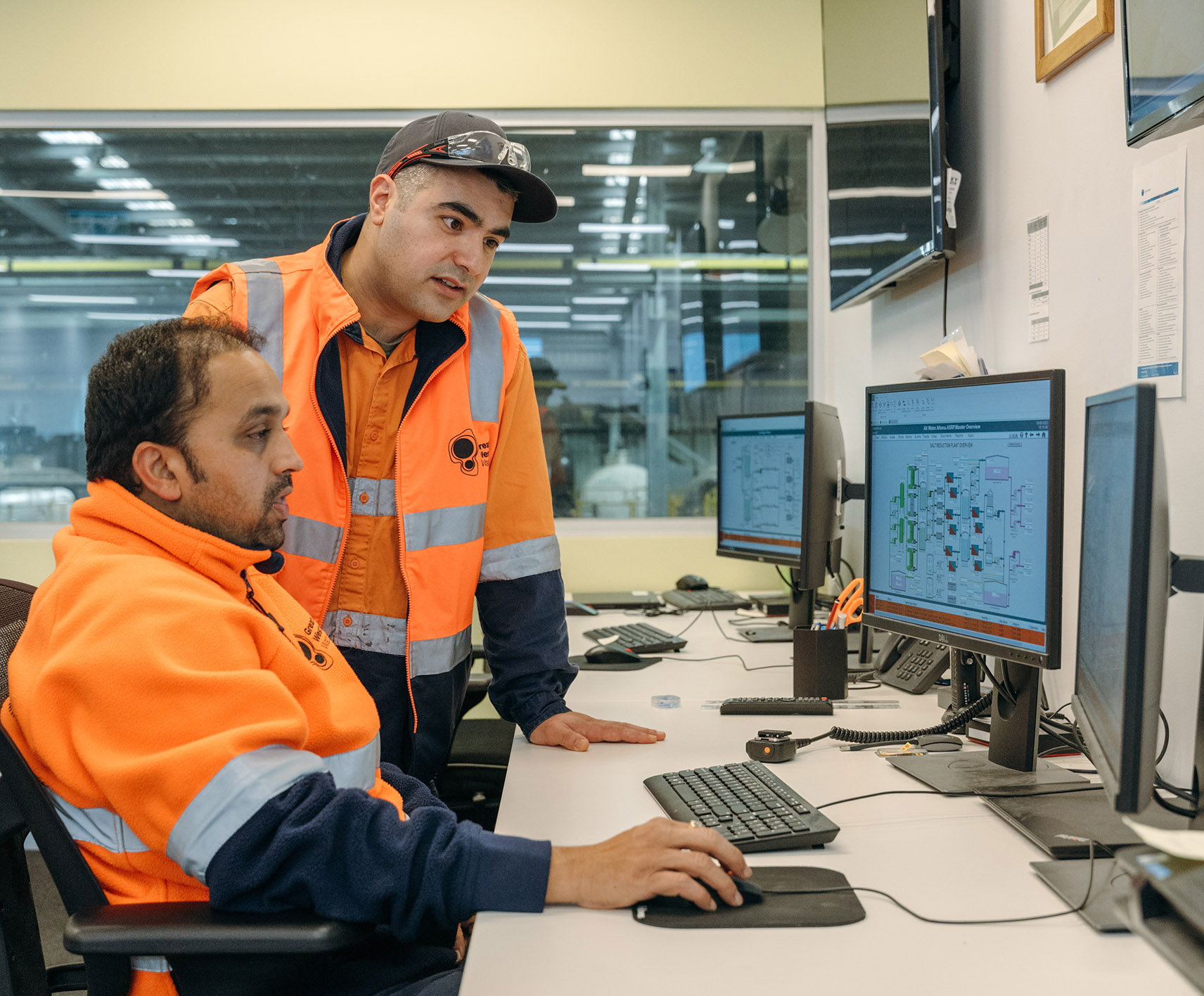 Two GWW workers, wearing protective gear looking at a computer screen.