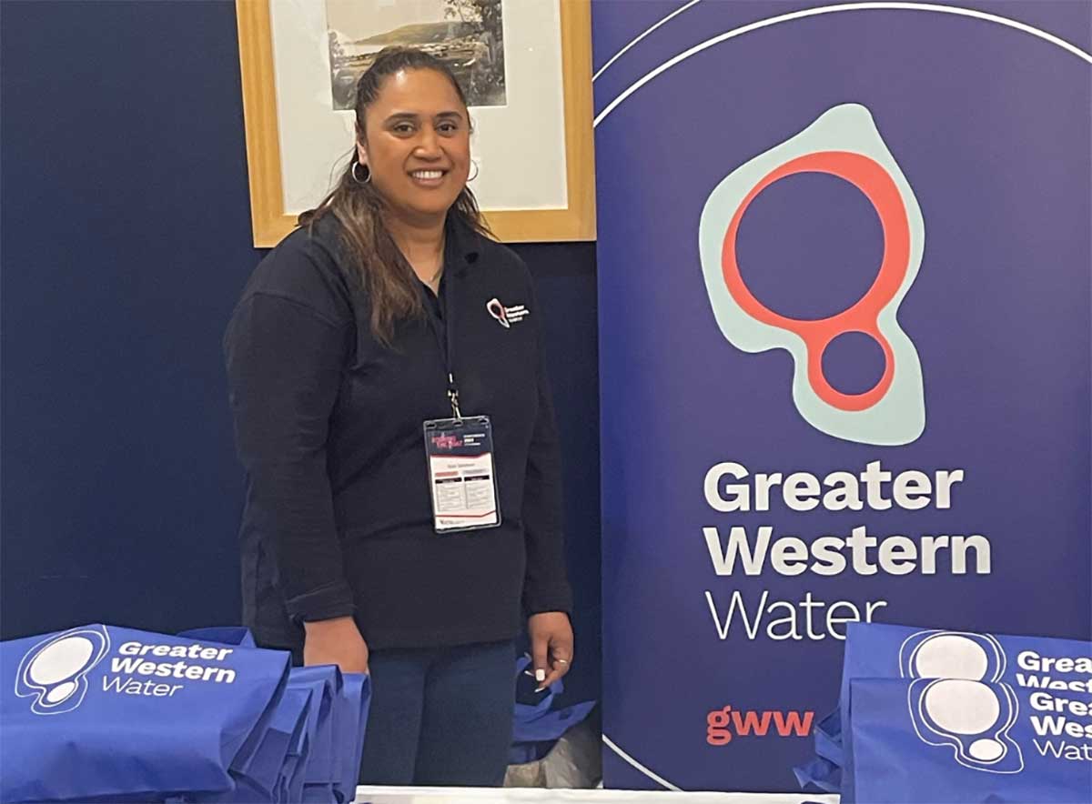 Sala wearing her corporate uniform in dark blue standing in front of a signboard bearing the GWW logo at a recent community information session.